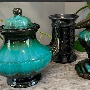 May include: A teal and black glazed ceramic teapot, a black ceramic incense burner with a decorative design, and a teal and black glazed ceramic pelican figurine.