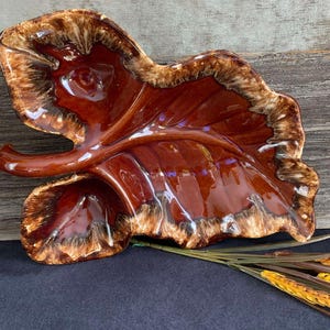 May include: A brown and white glazed ceramic leaf-shaped serving dish. The dish has a raised centre and a brown glaze with white streaks.