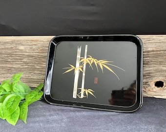 May include: Black lacquer serving tray featuring a gold bamboo design. The tray has a raised rim and a smooth surface.