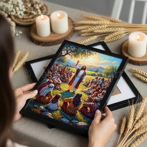 May include: A framed religious artwork depicts a biblical scene with a central figure in a white robe addressing a crowd. The artwork features vibrant colors, with a focus on the central figure and the surrounding landscape. The frame is black.