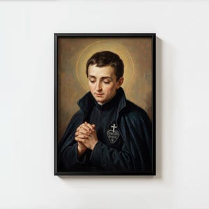 May include: Framed portrait of a man with dark hair, wearing a black cloak and a white emblem with a cross and text. The man is depicted with his hands clasped in prayer, and a golden halo surrounds his head. The artwork is set against a neutral background.