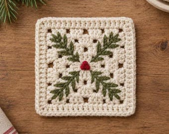 May include: A square crochet coaster in off-white yarn featuring a central embroidered design of four dark green pine sprigs arranged in a cross pattern with three small red berries at the center point of the intersection.