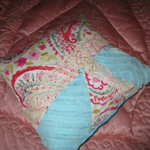 May include: A patchwork pillow with a blue, pink, and white floral design. The pillow is made of different fabrics, including a soft, fluffy material and a lace trim.