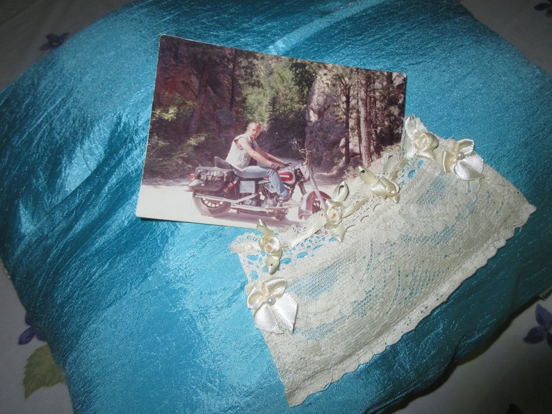 May include: A blue satin pillow with a white lace trim and a photo of a person riding a motorcycle in a wooded area.