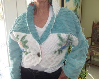 May include: A blue and white crocheted jacket with a ruffled collar and floral embroidery. The jacket is made of a soft, textured fabric.
