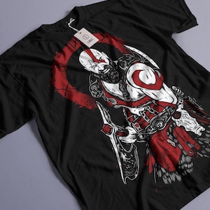 May include: Black t-shirt with a white graphic of Kratos from the God of War video game series. The graphic shows Kratos holding a weapon and has a red background.