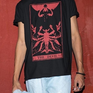 May include: Black t-shirt with a red graphic of the Devil card from a tarot deck. The card features a red demon with wings and horns, and the text "THE DEVIL".
