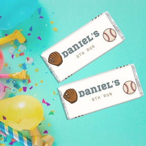 May include: Two white candy bar wrappers with baseball graphics. Each wrapper has a baseball glove, a baseball, and the text "Daniel's 8th Run" in dark grey. The background is teal with confetti and party decorations.