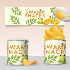 May include: Two cans of "Swamp Snacks" potato chips with a whimsical design featuring a frog, dragonfly, and leaves. The cans are filled with chips, and the label includes the text "Swamp Snacks". A banner with the same design is above the cans.