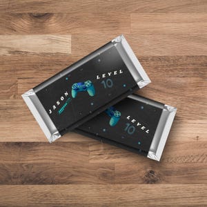 May include: Two black and silver chocolate bar wrappers with a blue and black video game controller graphic. The text "LEVEL 10" is on both wrappers. One wrapper has the name "JASON" on it.