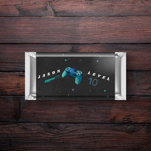 May include: A black and silver chocolate bar wrapper with a blue and green video game controller graphic. The wrapper has the text "JASON LEVEL 10" on it.