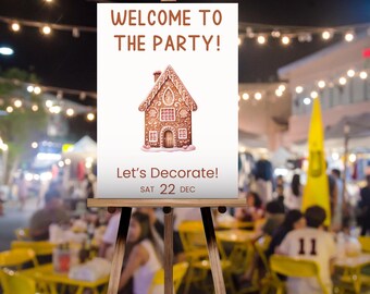 May include: A white sign with the text "Welcome to the party!" and a gingerbread house illustration. The sign also says "Let's Decorate!" and "Sat 22 Dec". The sign is on a wooden easel.