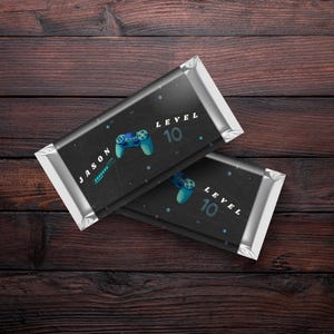 May include: Two black chocolate bar wrappers with silver foil. The wrappers have a black and white design with a blue video game controller and the text "Level 10". One wrapper has the name "Jason" on it.