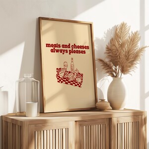 Framed retro kitchen print with bold red typography 'meats and cheeses always pleases' and a charcuterie basket illustration.
