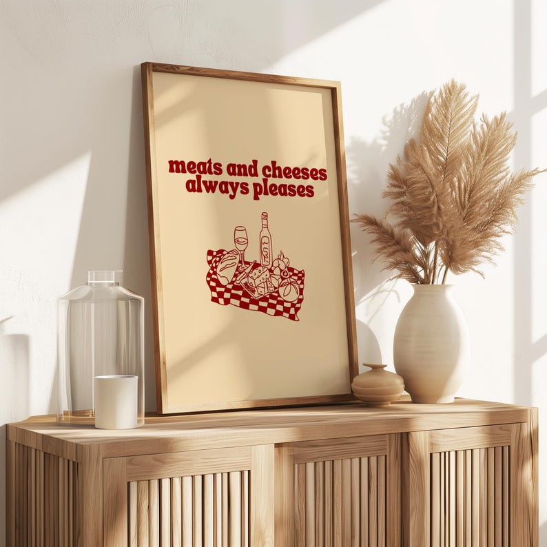 Framed retro kitchen print with bold red typography 'meats and cheeses always pleases' and a charcuterie basket illustration.