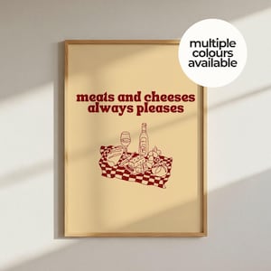 May include: A framed wall art print with a light beige background featuring dark red text that reads "meats and cheeses always pleases" above a line drawing of a picnic scene with a bottle, glass, bread, and cheese on a checkered cloth.