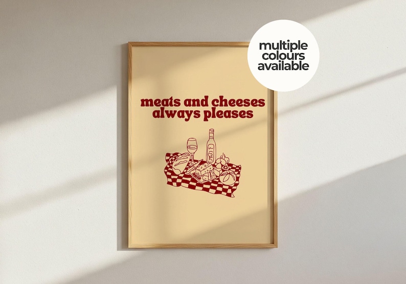 May include: A framed wall art print with a light beige background featuring dark red text that reads "meats and cheeses always pleases" above a line drawing of a picnic scene with a bottle, glass, bread, and cheese on a checkered cloth.