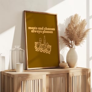 A framed mustard yellow print featuring white text that reads meats and cheeses always pleases above an illustration of a charcuterie picnic.