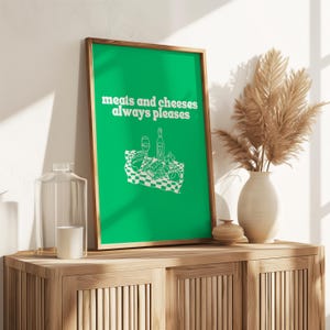 A framed vibrant green print showing white text that reads meats and cheeses always pleases alongside a charcuterie picnic graphic.