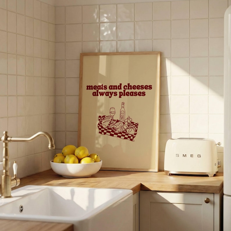 May include: A rectangular framed wall art print with a cream background and dark red text that reads meats and cheeses always pleases. Below the text is a dark red line drawing of a picnic spread with a wine bottle, glass, and food items.