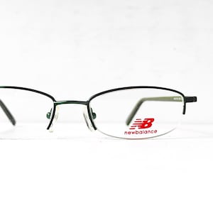Puede incluir: Gafas de metal con montura verde y lentes transparentes. El nombre de la marca "newbalance" está impreso en rojo en la lente derecha.