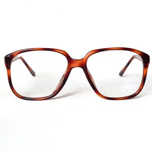 May include: Brown tortoiseshell eyeglasses with a square frame. The glasses have a classic design with a thick frame and clear lenses. The arms of the glasses are thin and attach to the frame at the top corners.