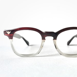 May include: Clear framed glasses with a burgundy and clear plastic frame. The glasses have a silver accent on the top of each arm.