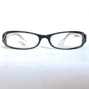 May include: Black reading glasses with a white swirling line pattern on the outer frames. The lenses are clear and feature a small white sticker with the text +2.50 printed in black on the right lens. The temples are white and translucent.
