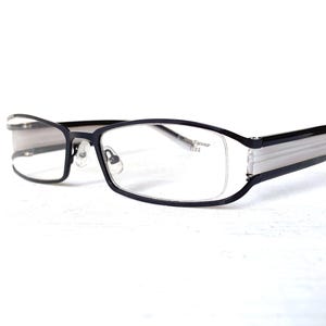 May include: Black rectangular eyeglasses featuring a thin frame and clear lenses. The temples display a white striped pattern on the side. The right lens has the text "Finesse Eyewear" printed in small black letters near the upper corner.