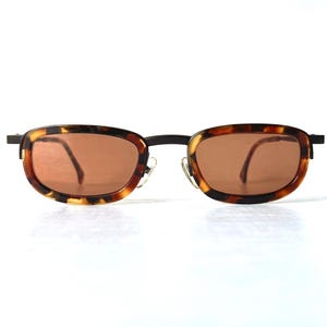 May include: Rectangular sunglasses with a tortoiseshell pattern frame and brown lenses. The frame has a dark metal bridge and temples. The sunglasses are set against a white background.