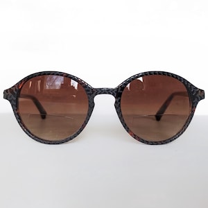 May include: Round-framed sunglasses with a patterned dark brown and black design. The lenses are a gradient brown color. The sunglasses have a classic, timeless style.
