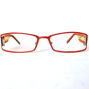 May include: Rectangular eyeglasses with a bright red metal frame. The temples feature a multi-colored horizontal striped pattern in shades of orange, yellow, and brown. The clear lenses are held by a thin red wire along the bottom edge.