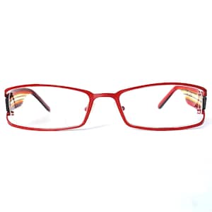 May include: Red rectangular eyeglasses with clear lenses. The frames have a thin, modern design. The temples feature a striped pattern in shades of orange, yellow, and brown. The glasses are set against a white background.
