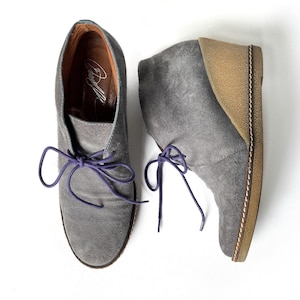 May include: A pair of gray suede ankle boots with purple laces. The boots have a wedge heel and a brown leather sole.