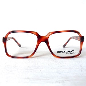 May include: Brown tortoiseshell eyeglasses with a square frame. The glasses have a keyhole bridge and thin temples. The text "BROADWAY Collection" is printed on the lower right lens.