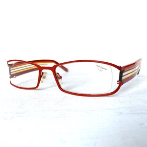 May include: Red eyeglasses with a multi-colored stripe design on the arms. The text "Anne et Valentin 1.25" is printed on the right lens.