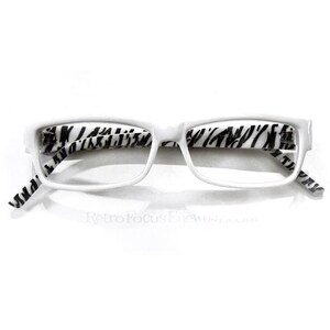 May include: White-framed eyeglasses with zebra print temples. The rectangular frames have a clean, modern design. The zebra print adds a bold contrast to the white frames. The glasses are set against a white background.