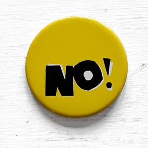 May include: A round, yellow button with the word "NO!" in bold, black letters. The exclamation point is white. The button is set against a white, textured background.