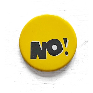 May include: A yellow button with the word "NO!" in black, bold letters. The exclamation mark is white with a black dot. The button is round and has a glossy finish.