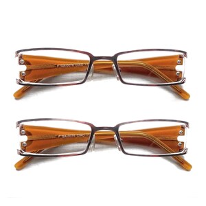May include: Two pairs of eyeglasses with rectangular frames. The frames are a mix of brown and reddish-brown, with orange-tinted lenses. The temples are a light brown color. The text "GA-0076 CIAO +1" is printed on the frame.
