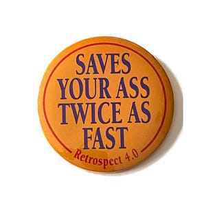 May include: A round, orange button with a red border and the text "SAVES YOUR ASS TWICE AS FAST" in purple. The text "Retrospect 4.0" is at the bottom. The button is set against a white background.