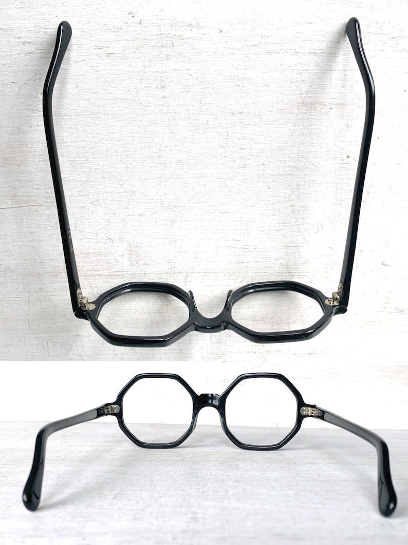 Puede incluir: Gafas negras octogonales con puente de cerradura y patillas curvas. Las gafas se muestran desde dos &aacute;ngulos diferentes sobre un fondo blanco. Las monturas son de color negro brillante y las lentes son transparentes.