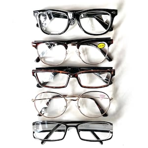 Puede incluir: Cinco pares de gafas están dispuestos verticalmente sobre un fondo blanco. Las monturas son negras, marrones y doradas, con varias formas, incluyendo rectangulares, redondas y de ojo de gato. Algunas gafas tienen etiquetas +2.00.