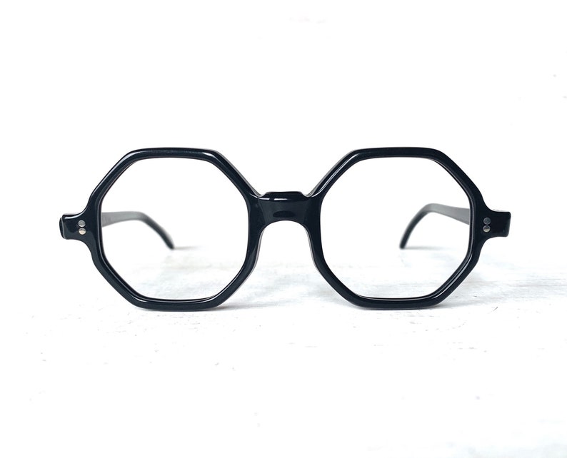 Puede incluir: Gafas negras de forma octogonal con lentes transparentes. Las monturas son de color negro brillante y las varillas son finas y oscuras. Las gafas tienen un dise&ntilde;o geom&eacute;trico moderno, adecuado para el uso diario.