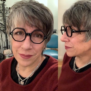 Puede incluir: Gafas negras de forma octogonal con montura gruesa. Las gafas las lleva una persona con pelo corto y gris y un jersey granate. Tambi&eacute;n se ve un collar plateado.