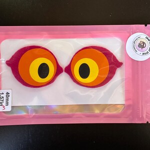 May include: Two felt eye-shaped appliques in a pink plastic pouch. Each eye features concentric circles of magenta, orange, yellow, and black. A white sticker on the pouch reads 40mm 1.57in, and a circular logo sticker reads Crafting Iggy Style.