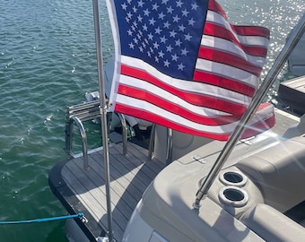 May include: A white boat with a wooden deck and a stainless steel flagpole holding an American flag. The boat is moored in a marina with other boats in the background.