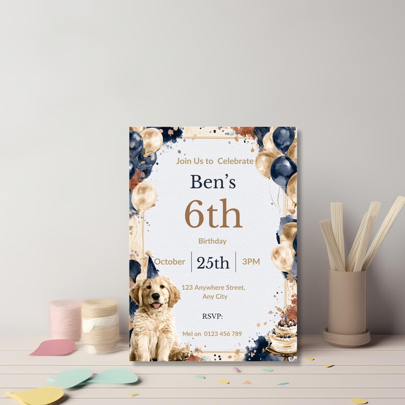 Watercolor dog birthday invitation leaning against a wall with craft thread and wooden sticks, navy and gold styling