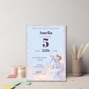 Fairytale princess birthday invitation leaning against a gray wall on a pastel desk with paper cutouts