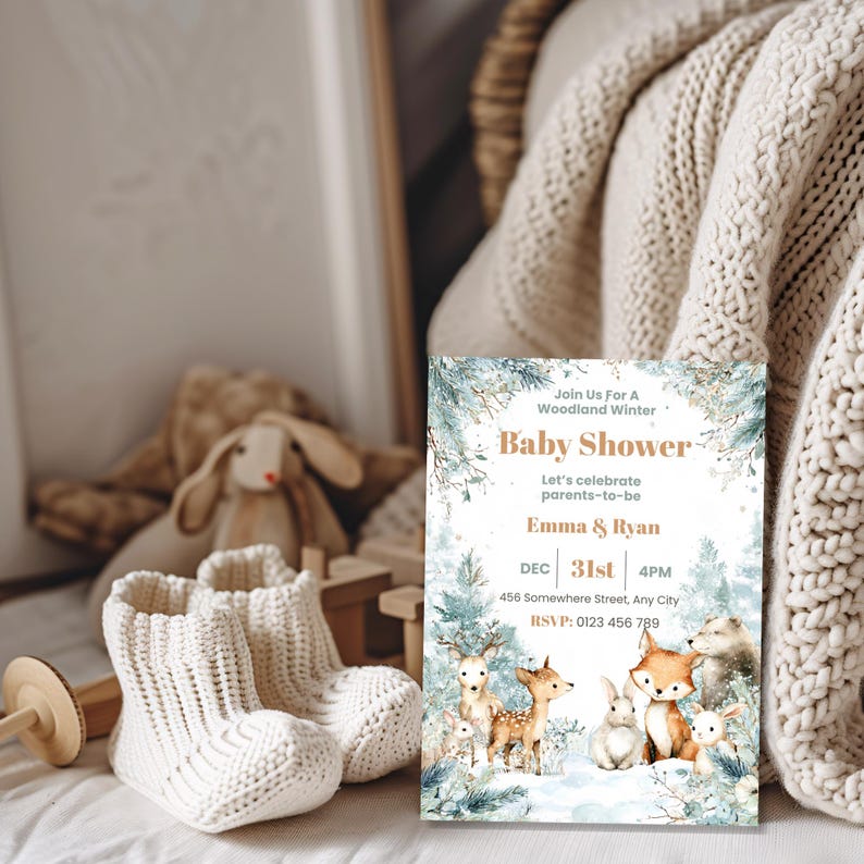 Woodland baby shower invitation displayed with knit baby booties and plush bunny, winter forest animal theme
